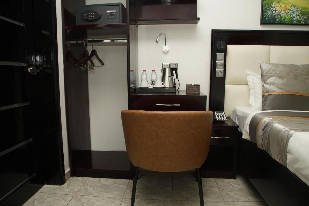 Ein Hotelzimmer mit einem Bett, einem Schreibtisch mit Kaffeemaschine, einem Sessel, einem Kleiderschrank und einem Bild an der Wand.