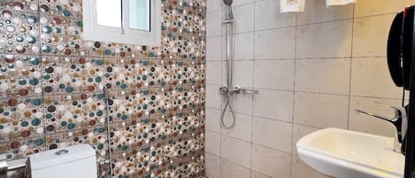 Un baño con pared de mosaicos, inodoro, ducha y lavamanos.