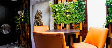 A modern room with a round table and two orange chairs, a decorative horse head, and a wall with vertical wooden slats and green plants.