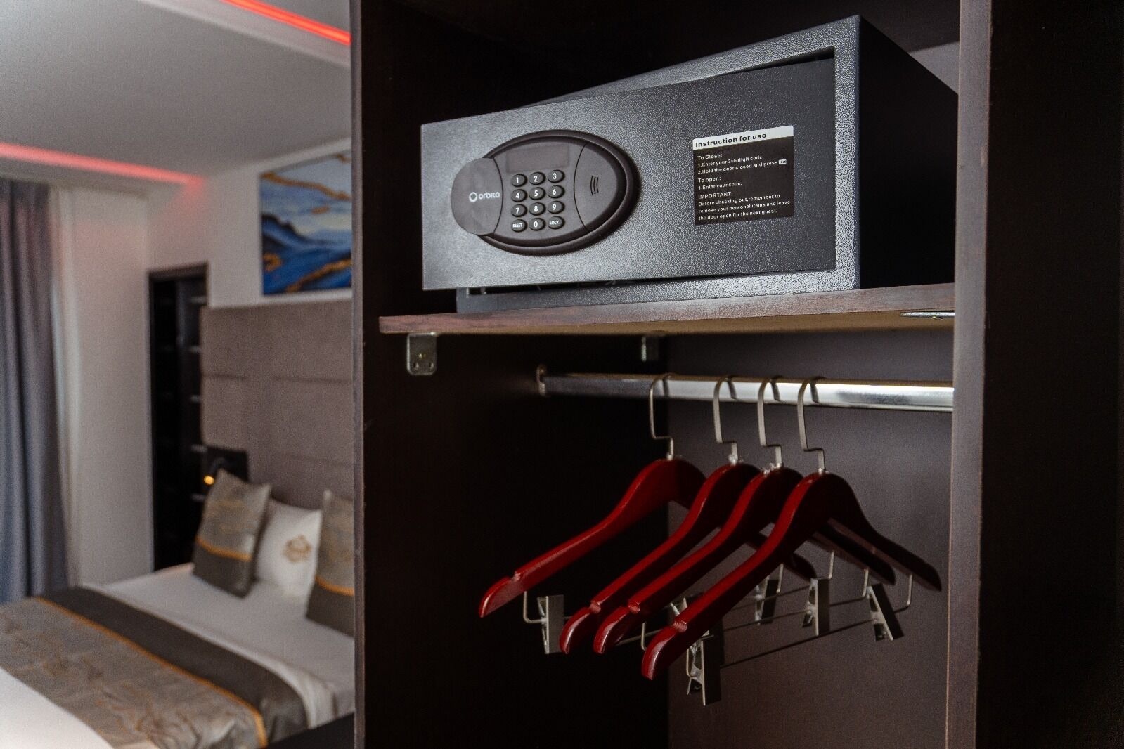 Ein Hotelzimmer mit Minibar, einem Bett und einem Kleiderhaken mit roten Kleiderbügeln.