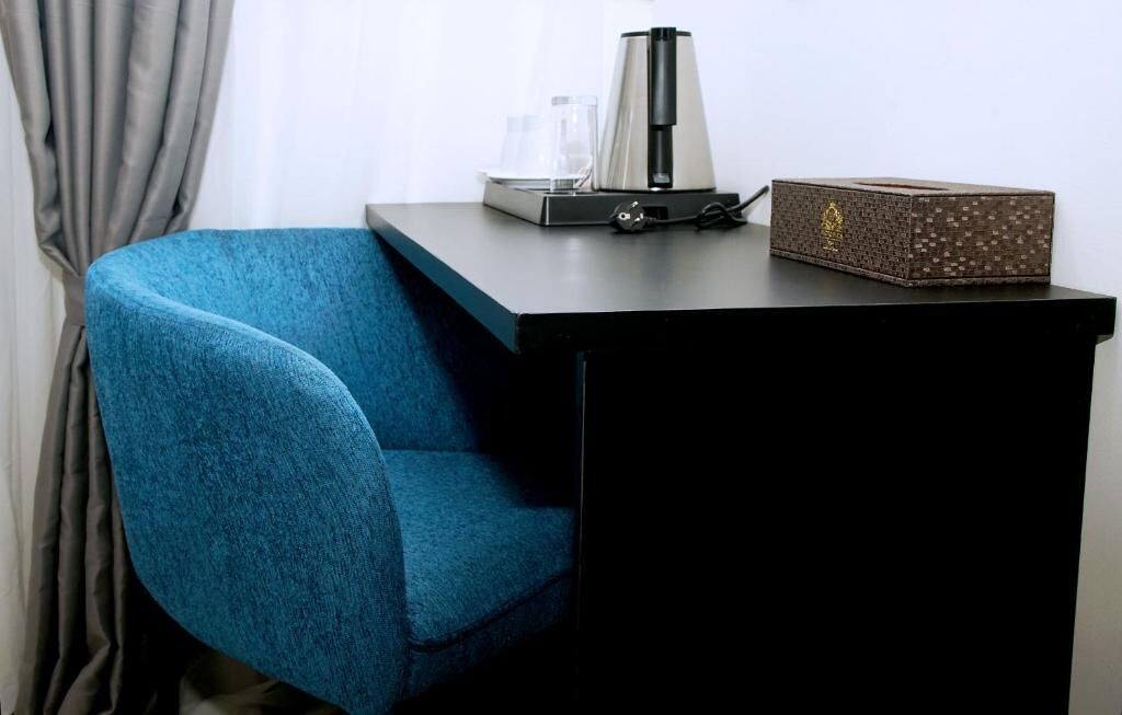 A corner of a room with a blue chair, a black table, a coffee maker, and a decorative box.