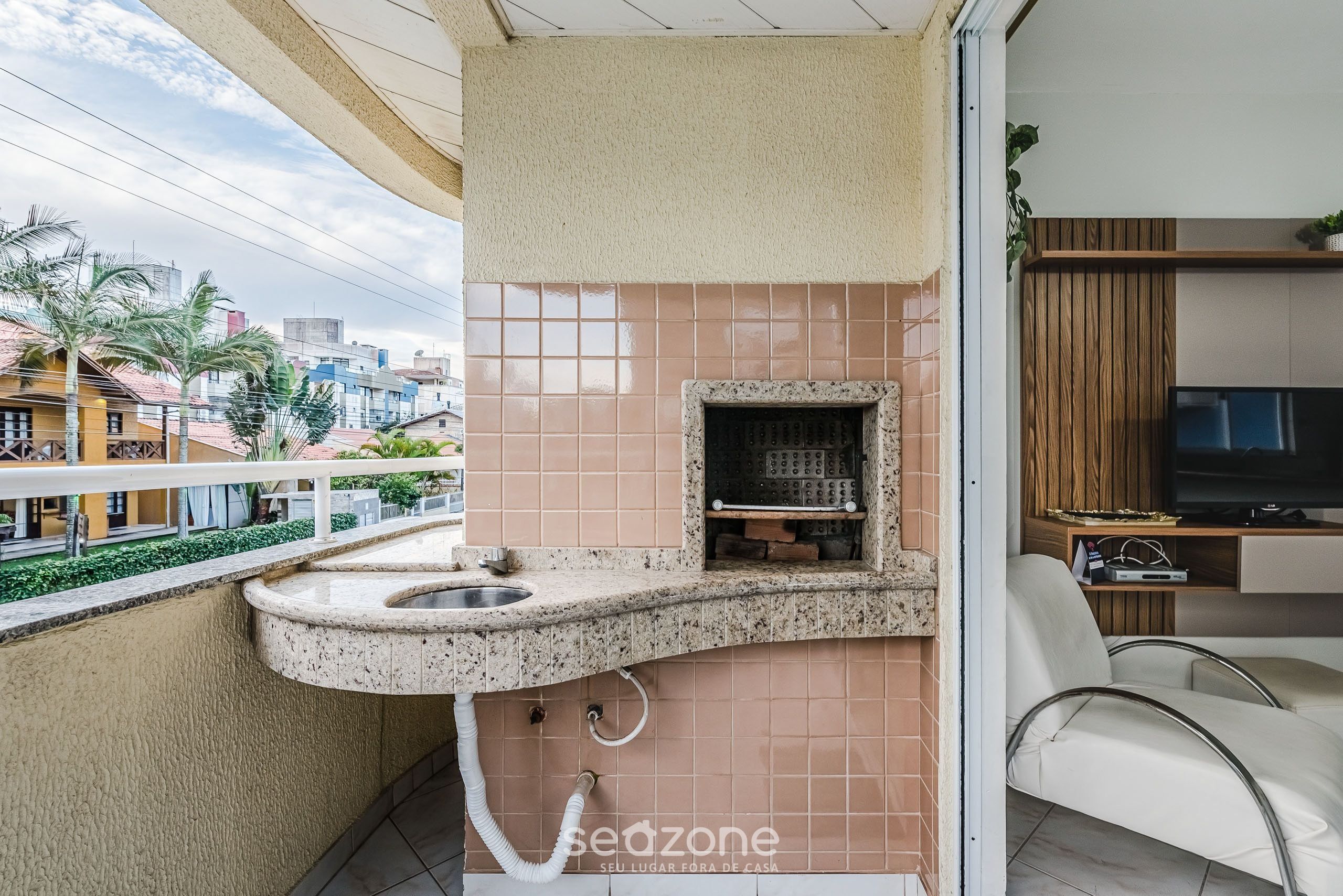 A balcony with a kitchen area, including a sink and a built-in grill, overlooking a residential area.