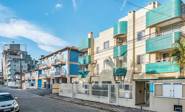 Una hilera de edificios residenciales con balcones, una calle pavimentada y un coche estacionado.