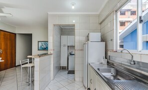 Een kleine keuken met een spoelbak, een koelkast en een eethoek met een stoel.