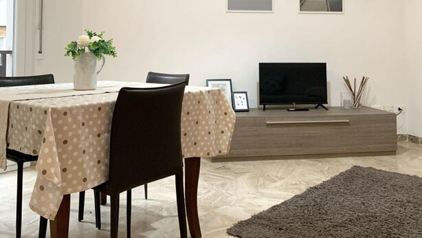 Een moderne eetruimte met een tafel voor twee personen, een televisie op een standaard en kunst aan de muur.