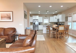 A modern kitchen with white cabinets, a stainless steel refrigerator, and a dining area with wooden chairs and a table. - You're in Heaven #198 - Boat Dock, Pool, Hot Tub, Dog Friendly, Sleeps 9! (Topsail Beach)