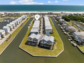 A marina with multiple boats docked, surrounded by residential buildings with balconies, and a view of the ocean in the background.