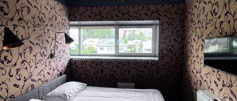 Un dormitorio con cama, ventana, candelabro y papel tapiz estampado.