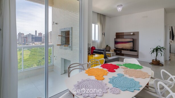 A modern living room with a balcony, a TV, and a table with colorful crocheted placemats. - Charm and Comfort 600m From the Beach! Etpa1103 (Porto Belo)