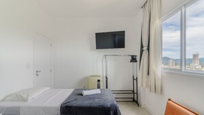 A hotel room with a bed, a TV mounted on the wall, a window with curtains, and a view of the cityscape. - Charm and Comfort 600m From the Beach! Etpa1103 (Porto Belo)