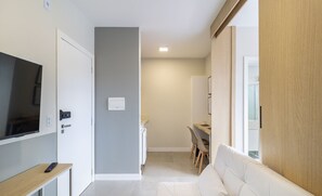 Uma sala de estar moderna com um sofá, uma TV sobre um móvel, e um espaço de refeições com cadeiras e uma mesa.