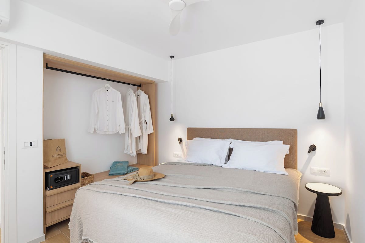 A bedroom with a bed, bedside table, nightstand, and a closet with hanging clothes.