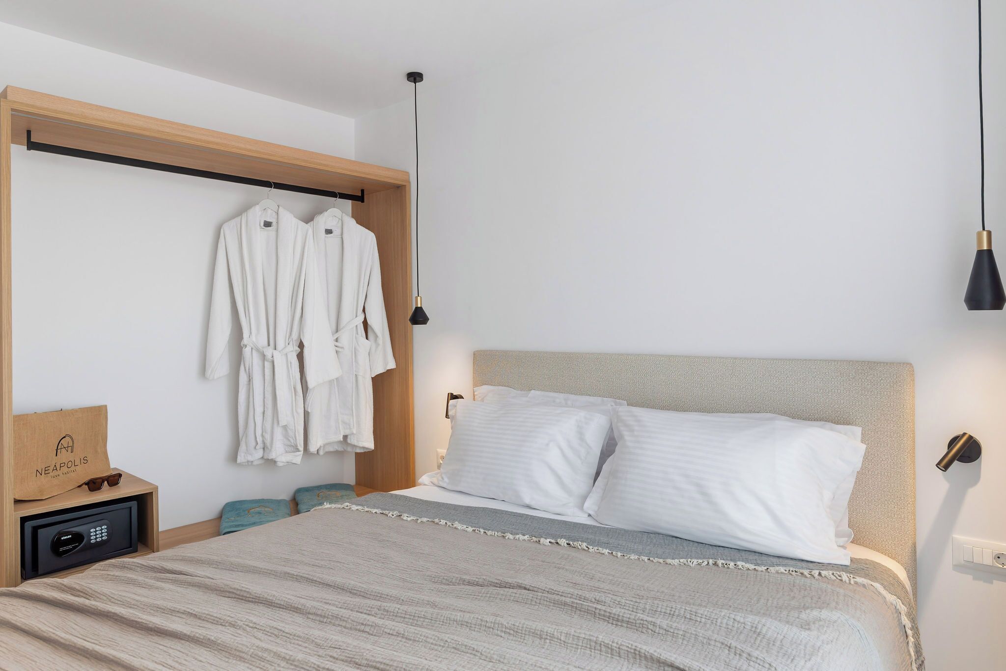 Une chambre à coucher moderne avec un lit, une table de chevet, un porte-manteau et une lampe suspendue.
