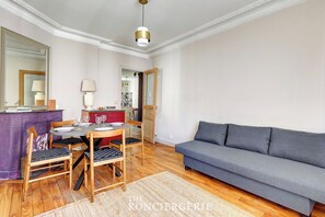 A living room with a grey sofa, wooden chairs, a dining table with chairs, a purple cabinet, and a mirror.