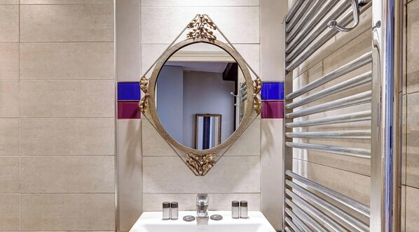 Un baño con un espejo grande y decorativo, un lavamanos con artículos de aseo y un perchero para toallas.