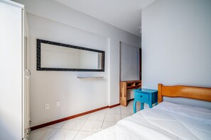 Une chambre à coucher avec un lit, une tête de lit en bois, une table de chevet bleue, une commode en bois, un miroir et un mur blanc.
