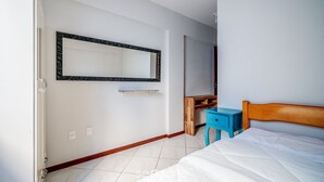 A bedroom with a bed, a wooden headboard, a blue nightstand, a wooden dresser, a mirror, and a white wall. - Apt W/barbecue 3 Minutes From Bombas Beach Fdl101 (Bombinhas)