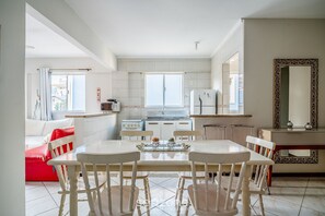 Une cuisine moderne avec des meubles blancs, une table à manger avec des chaises et une grande fenêtre.
