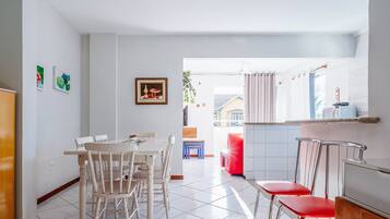 A dining area with a white table and chairs, a red chair, and a TV on a wooden stand.