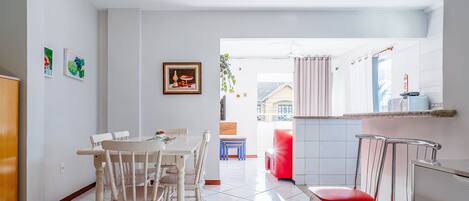 A dining area with a white table and chairs, a red chair, and a TV on a wooden stand.
