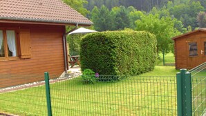 A wooden cabin with a tiled roof, a fenced yard, and a large hedge. - Charming Chalet in Plainfaing (Plainfaing)