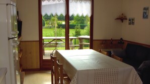 A kitchen with a dining table, chairs, a refrigerator, and a view of a garden through a large window. - Charming Chalet in Plainfaing (Plainfaing)