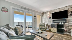 A living room with a sofa, armchairs, a coffee table, and a TV. There's a balcony with a view, and the room has a modern design with a wooden wall and a flat-screen TV mounted on it. - The Flamingo Balcony Waterview Heated Pool (Tampa)