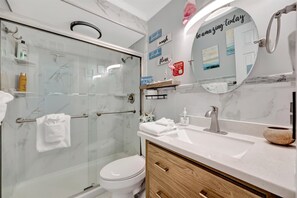 Une salle de bain moderne dotée d’une douche à parois de verre, de toilettes blanches, d’un meuble-lavabo avec un plan de travail en marbre et d’un miroir orné d’une citation inspirante.