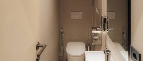 A modern bathroom with a toilet, sink, and shower. There are wall-mounted towel racks and a large mirror.