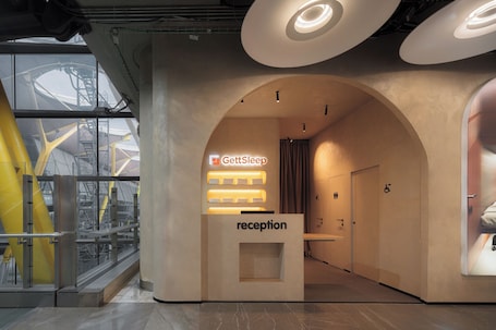 Un'area reception con il cartello GettSleep, una scrivania e vista su edifici industriali attraverso ampie finestre.. GettSleep Madrid Capsules - Terminal T4S, Departures