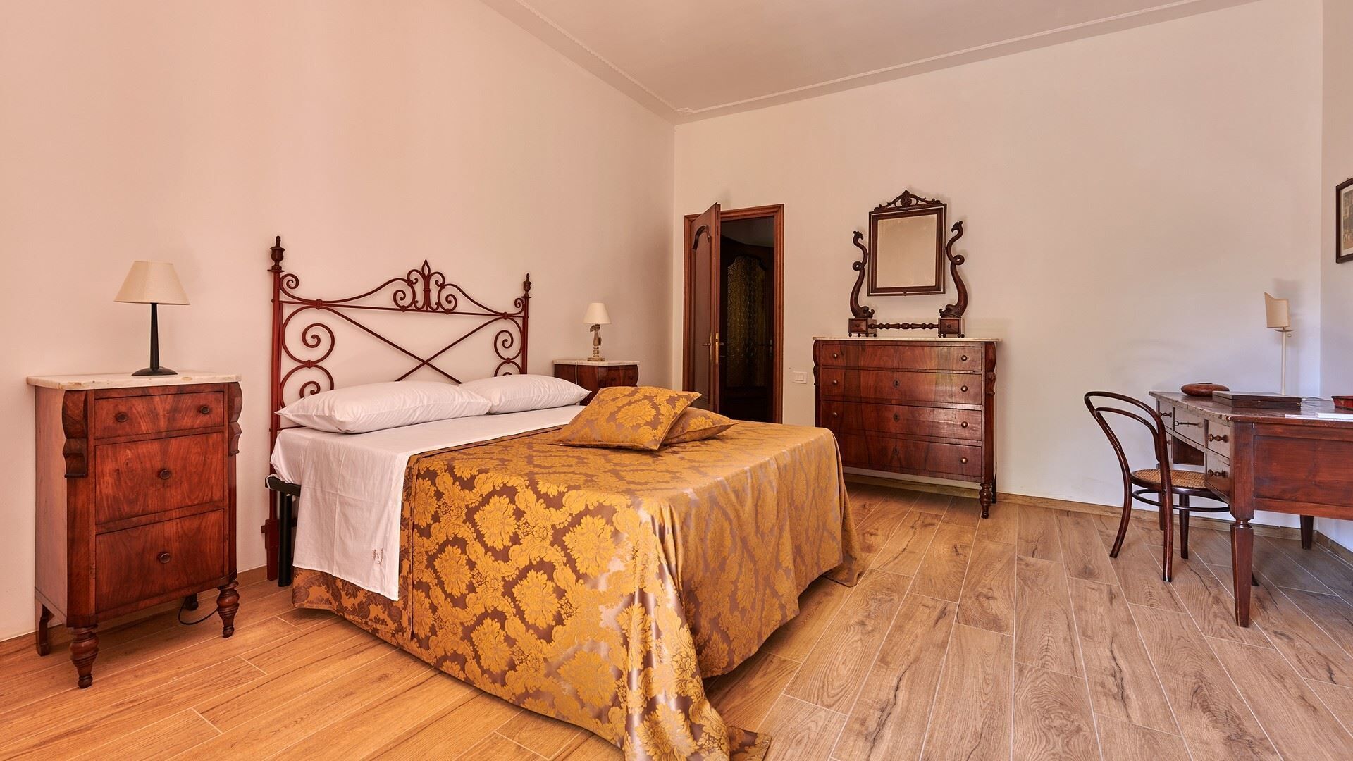 A bedroom with a bed, wooden dresser, desk, and a mirror.
