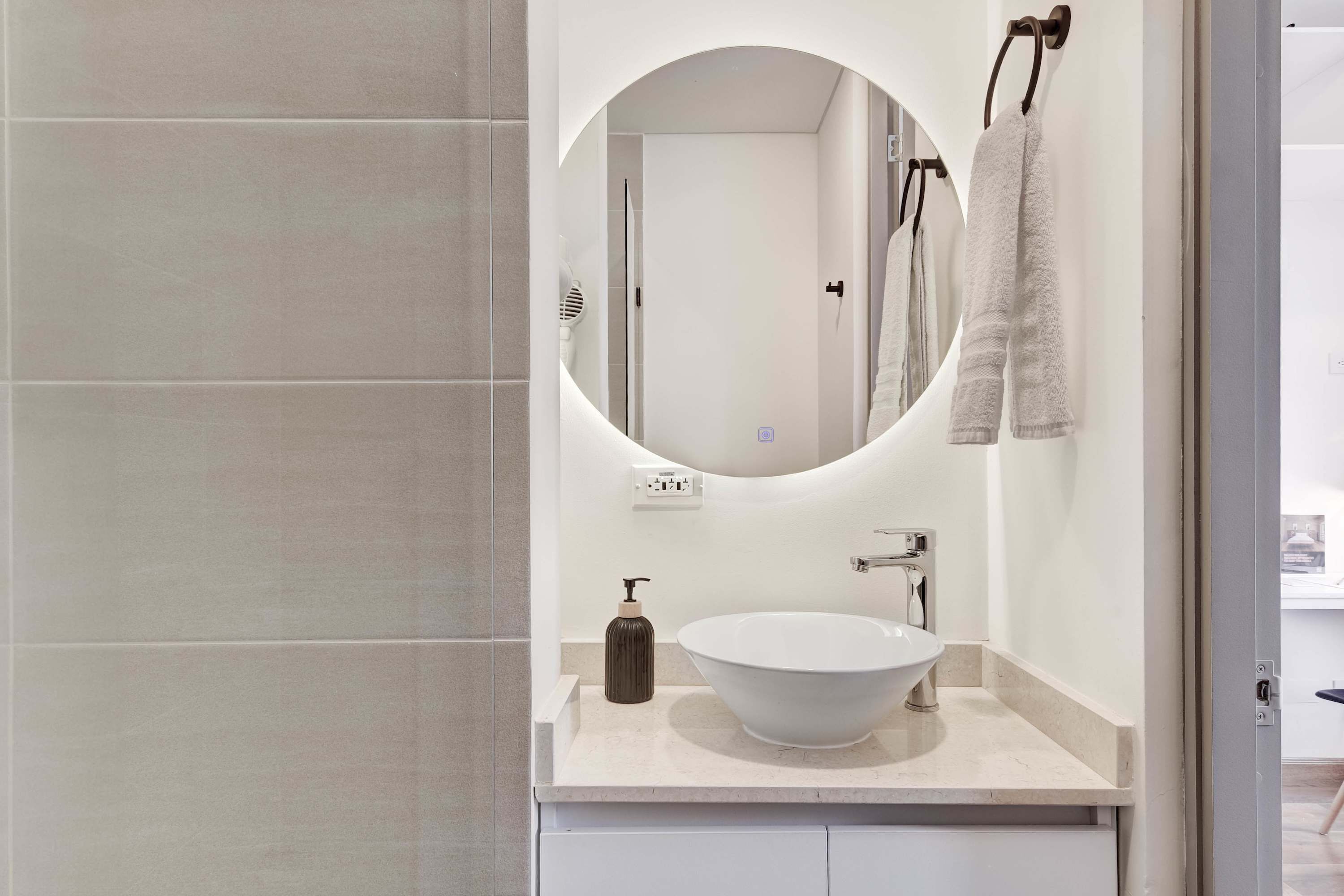 A modern bathroom with a round mirror, a white sink, and a towel rack.