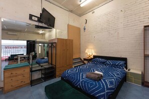 Un dormitorio con cama, armario, escritorio, silla, espejo y televisor.