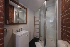 A modern bathroom with a glass shower enclosure, a white sink, and a mirror with a wooden frame. - Spacious Studio in Quiet Northcote Neighbourhood (Northcote)