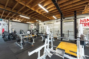 Un gimnasio con equipo de levantamiento de pesas, una prensa de banca y techo de madera.
