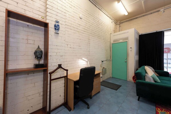 Una habitación con pared de ladrillo, un escritorio con silla, una puerta verde y un sofá verde.