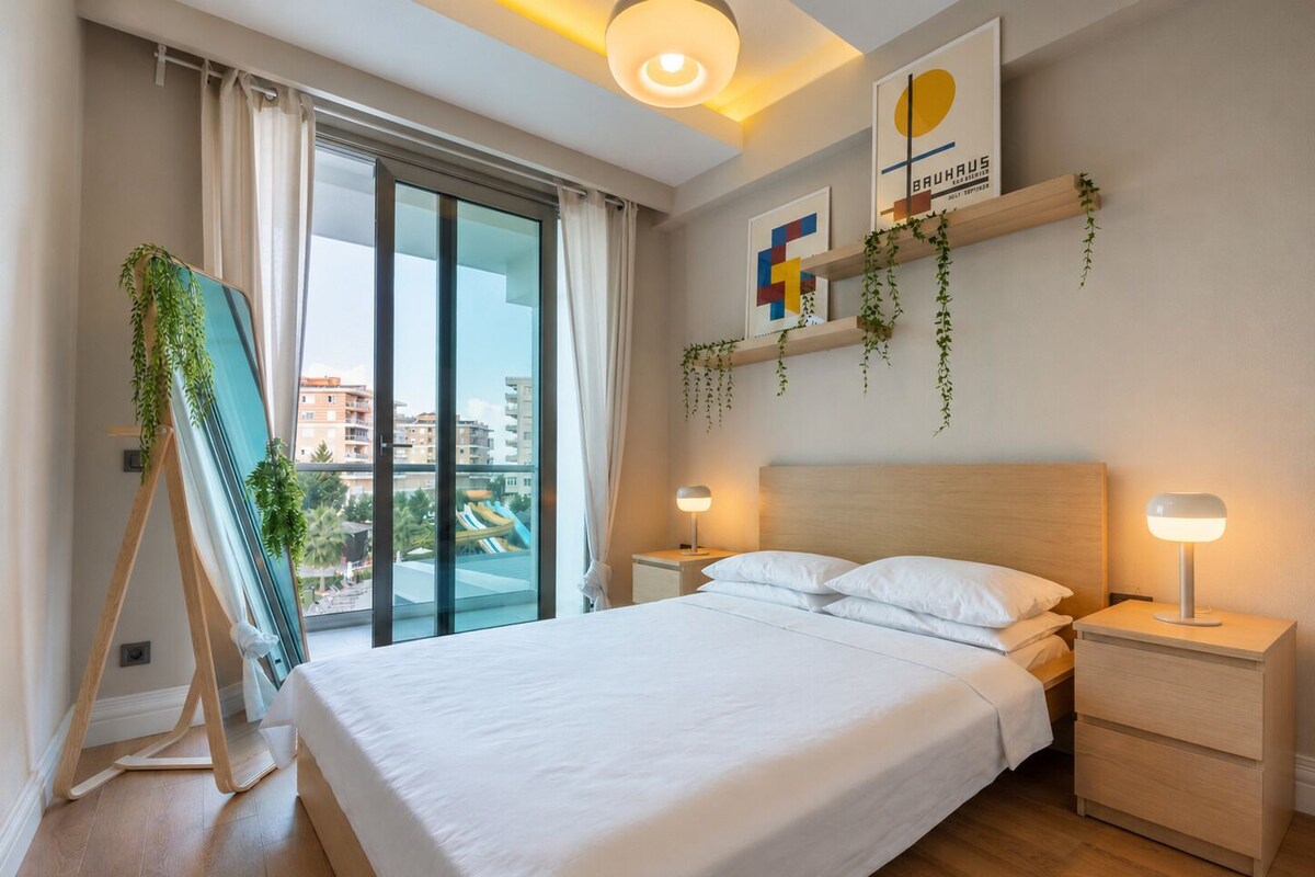 A modern hotel room with a large bed, bedside tables, a view of a cityscape, and a ceiling light fixture.