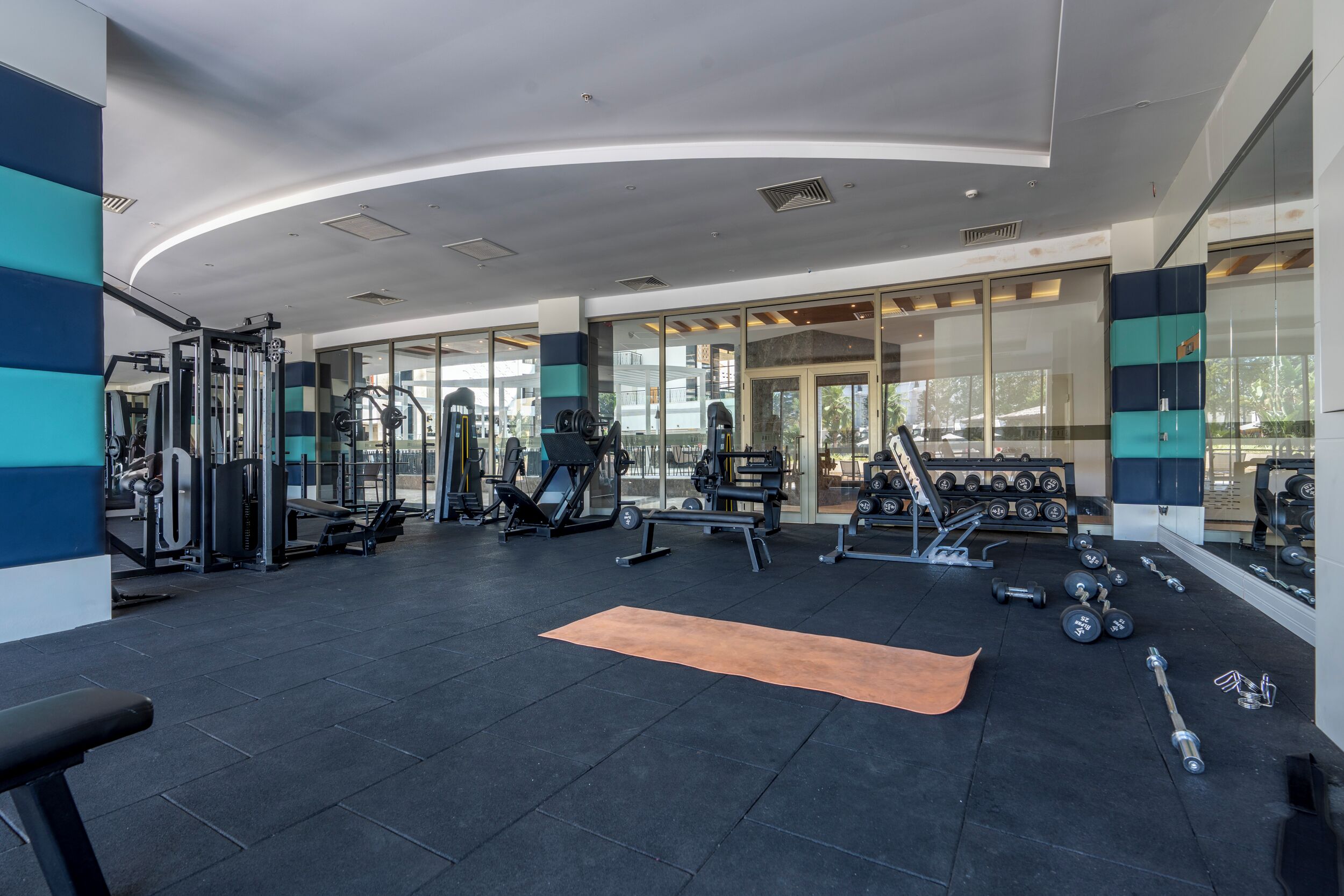 Un gimnasio moderno con diversos equipos de ejercicio, un espejo grande y una colchoneta en el suelo.