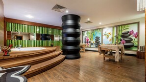 A modern spa area with a central circular seating area, a large black cylindrical sculpture, and a wall with vertical bamboo panels. - Maxihomes Sirella (Antalya)