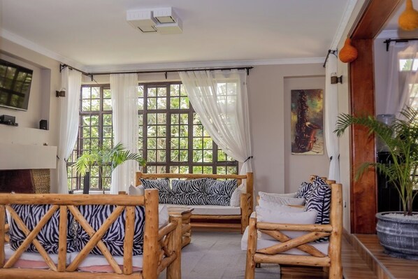 A room with a wooden bed, a sofa, and a large window with curtains. - Lux Suites Enkarsis Bungalow Kisaju (Kitengela)