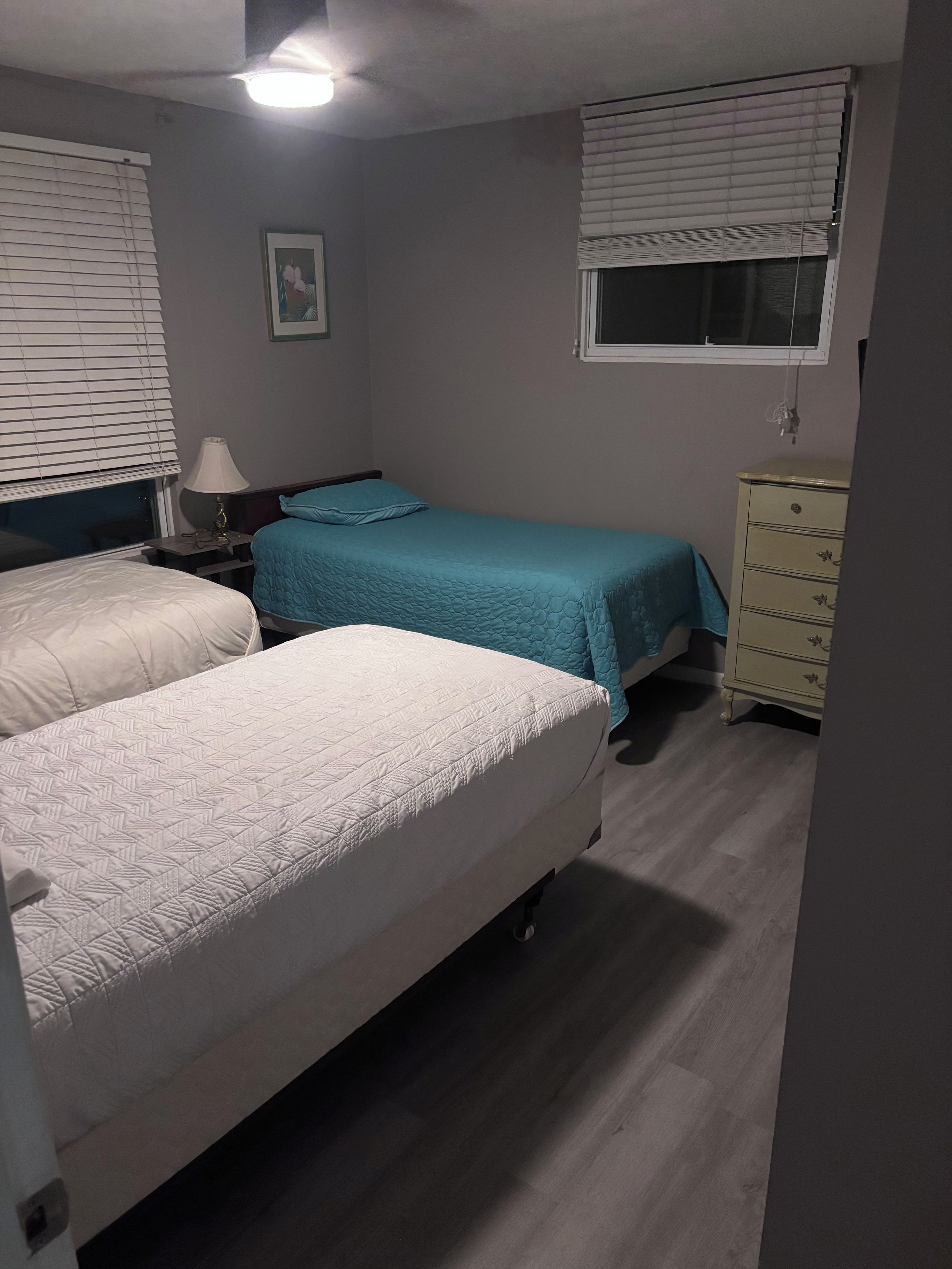A bedroom with two beds, a nightstand, a dresser, and a window with blinds.