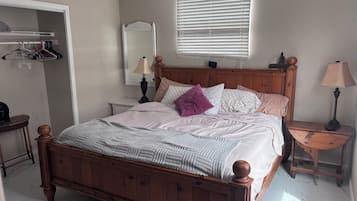 A bedroom with a wooden bed, a bedside table with a lamp, a mirror, a wardrobe, and a ceiling fan.