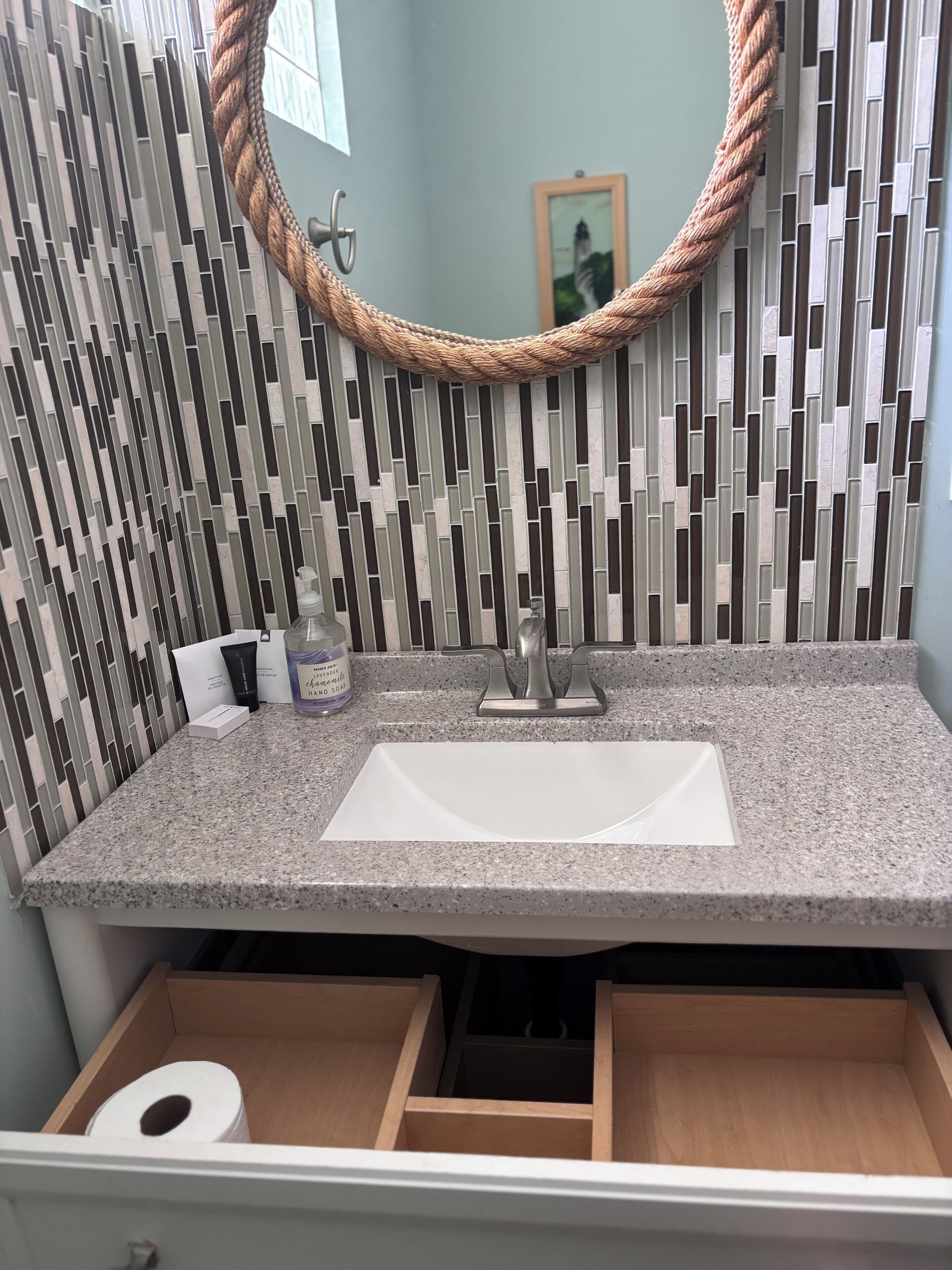 Une salle de bain dotée d’un comptoir en granit, d’un lavabo blanc, d’un miroir encadré d’une corde et d’un mur à motifs.