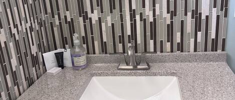 Une salle de bain dotée d’un comptoir en granit, d’un lavabo blanc, d’un miroir encadré d’une corde et d’un mur à motifs.