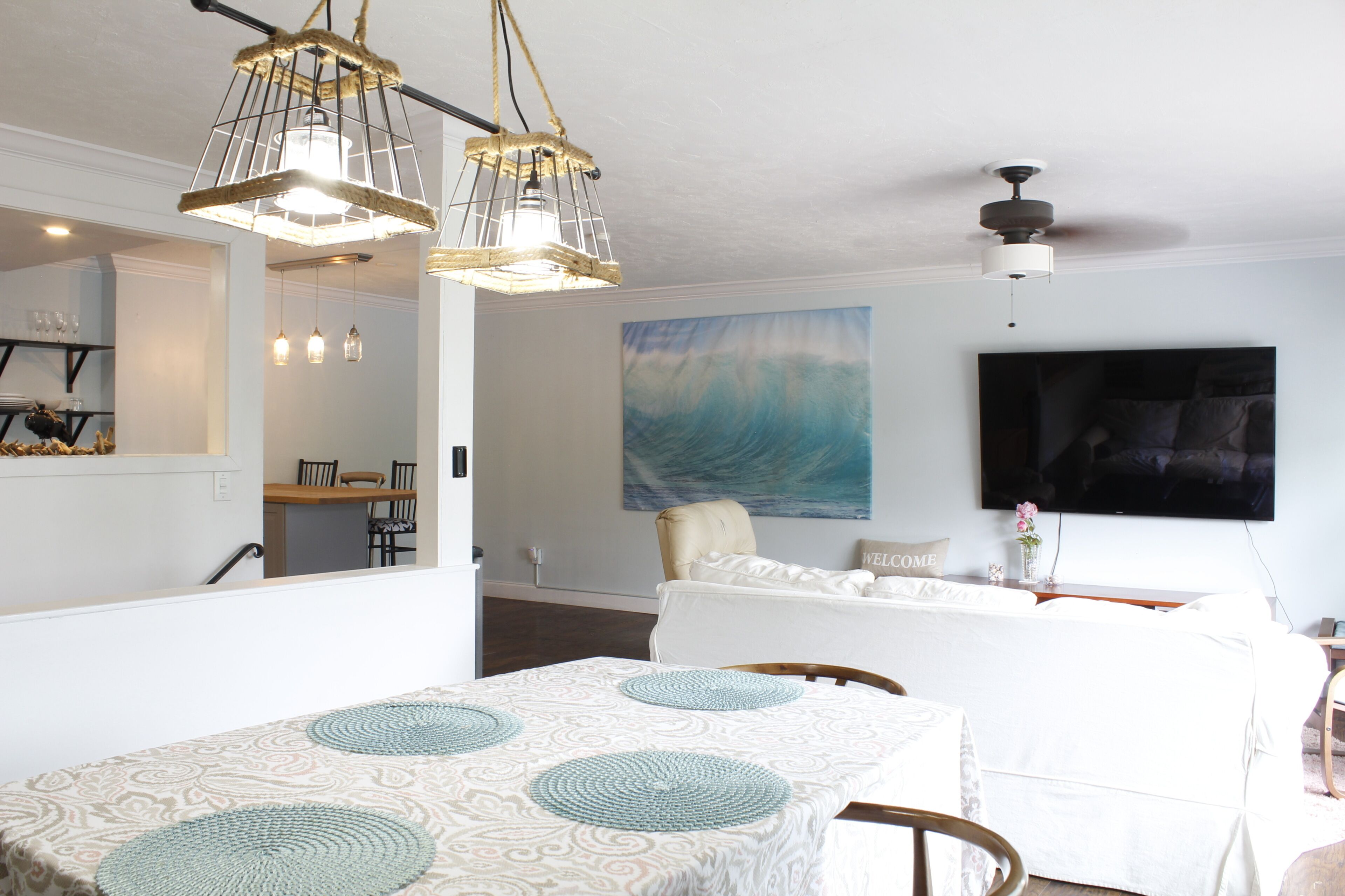 A modern living room with a dining area, a large painting, and a flat-screen TV.