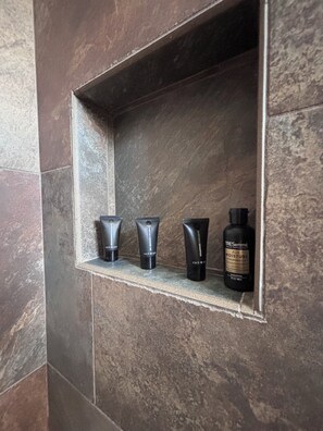 A bathroom shelf with four toiletries: two tubes of cream, one tube of lotion, and a bottle of shampoo.