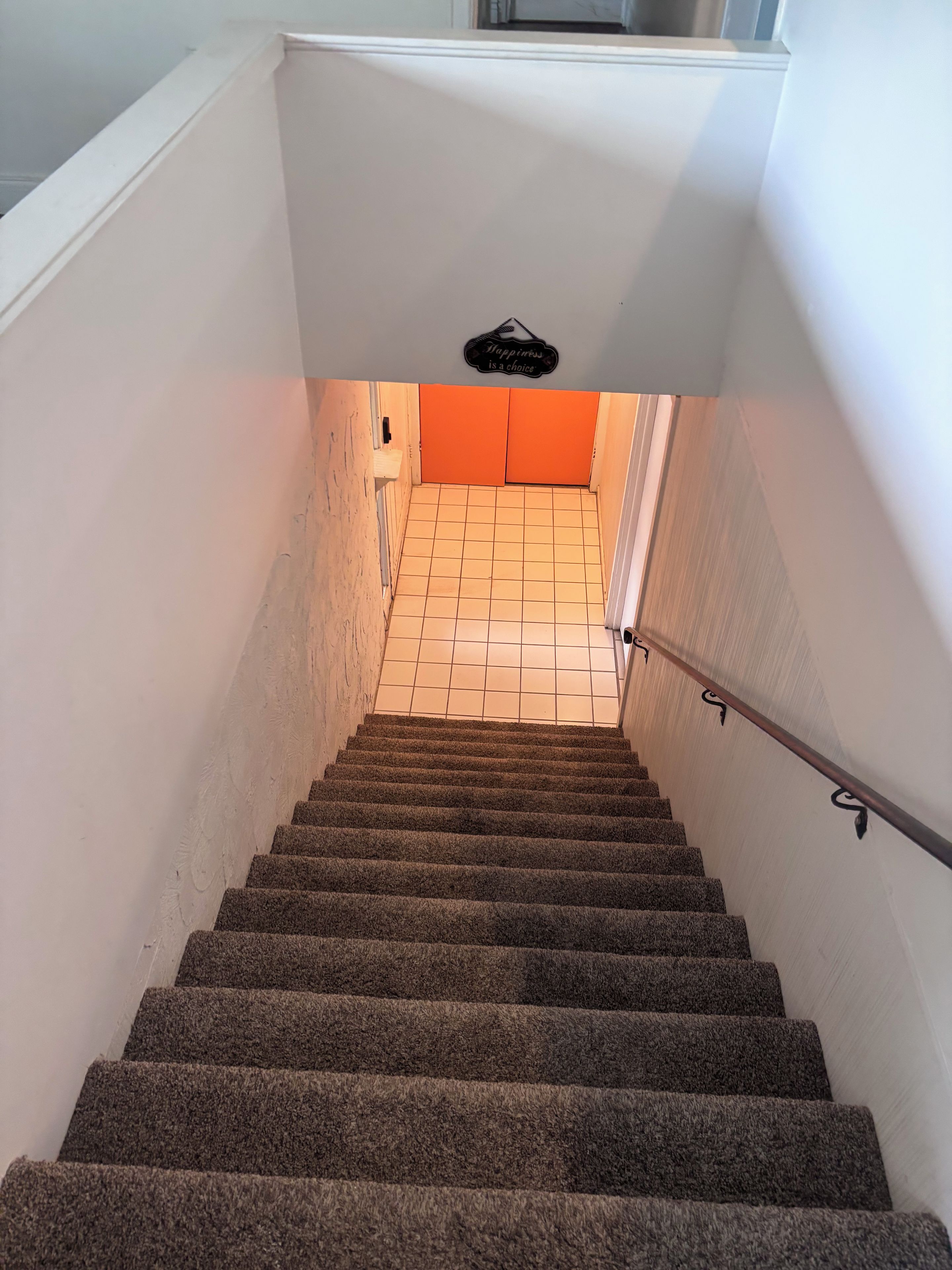A carpeted staircase leading to a room with a tiled floor and an orange door.