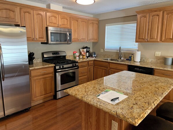 A kitchen with wooden cabinets, stainless steel appliances, granite countertops, and a window with blinds.