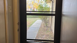 Puerta con vista a una calle residencial, aceras y una casa con follaje otoñal.