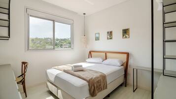 A bedroom with a large window, a bed with a wooden headboard, a bedside table, and a chair.